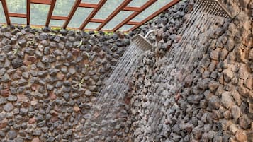 Una fuente de piedra con cascada, rodeada de plantas y una barandilla de metal.