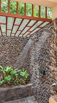 A stone water feature with a waterfall, surrounded by plants and a metal railing.