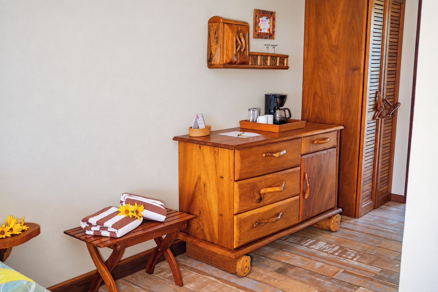 A wooden cabinet with drawers, a small table with towels, and a coffee maker on top.