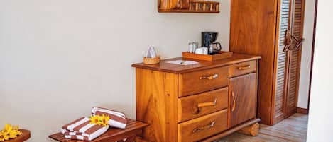 A wooden cabinet with drawers, a small table with towels, and a coffee maker on top.