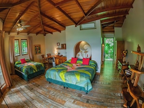 A room with two beds, a desk, and a chair. There is a ceiling fan and an air conditioning unit.