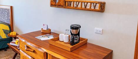 Un aparador de madera con cajones, una cafetera y una bandeja con tazas y una cesta.