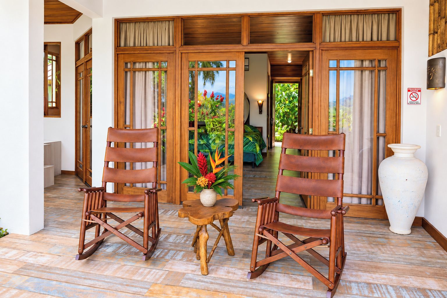 Une pièce aux murs en bois, avec deux fauteuils à bascule et une table, un grand vase, et une vue sur un jardin luxuriant.