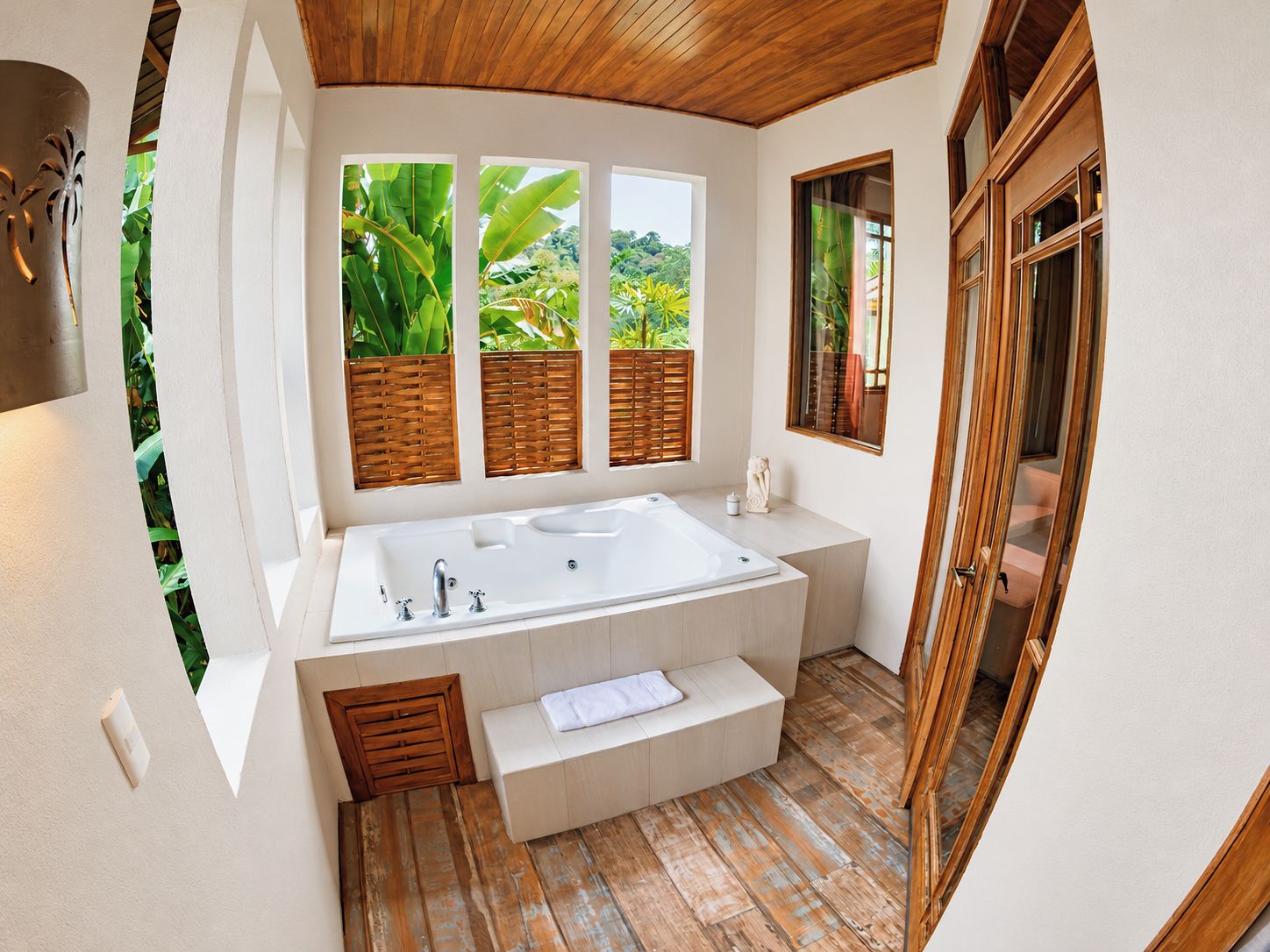 A modern bathroom with a large bathtub, wooden slatted windows, and a view of lush greenery.