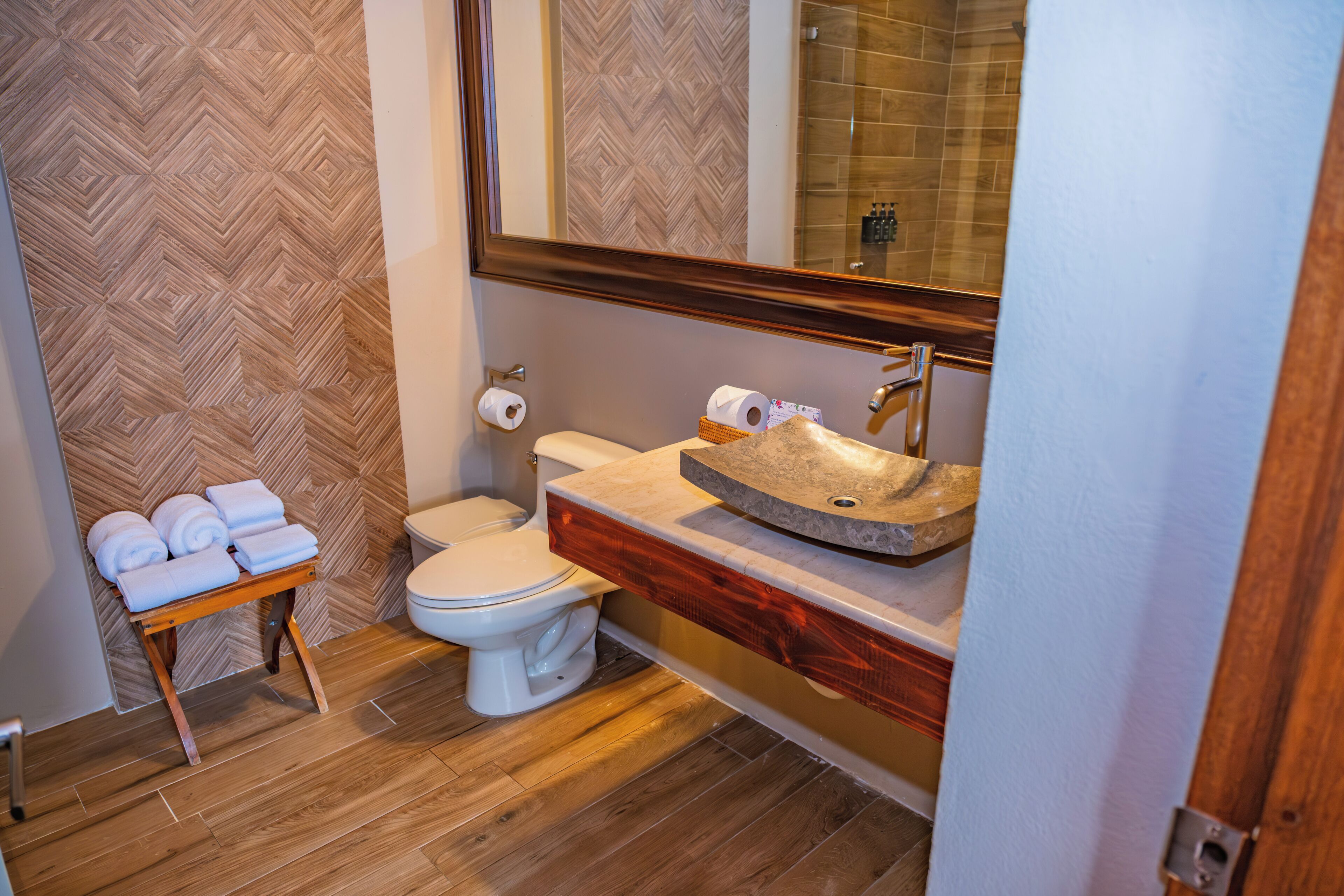 A bathroom with a wooden herringbone floor, a white toilet, a wooden vanity with a stone sink, and a mirror above the sink.