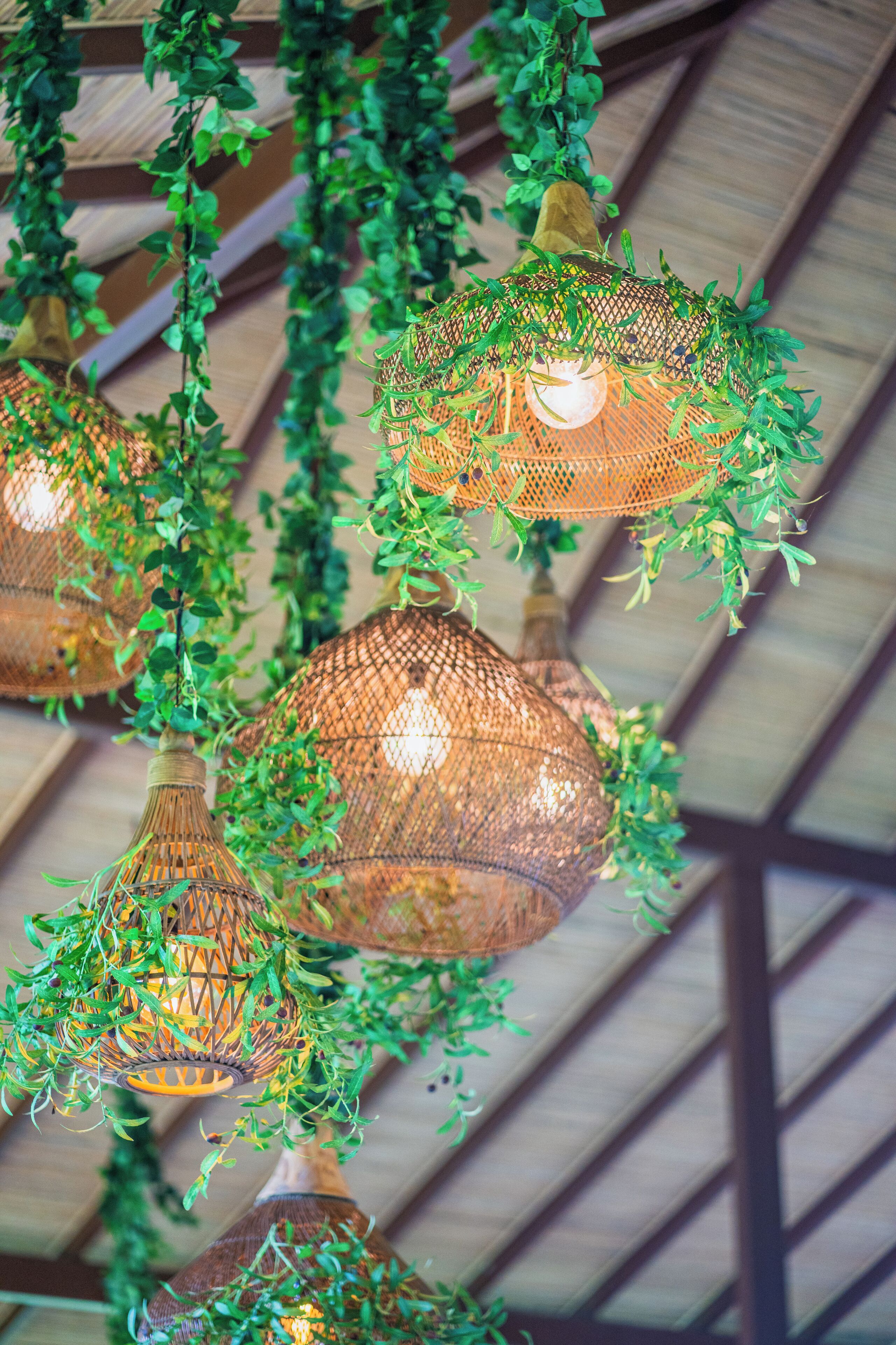 Hanging wicker lamps with greenery, set against a wooden ceiling structure.