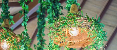 Hanging wicker lamps with greenery, set against a wooden ceiling structure.
