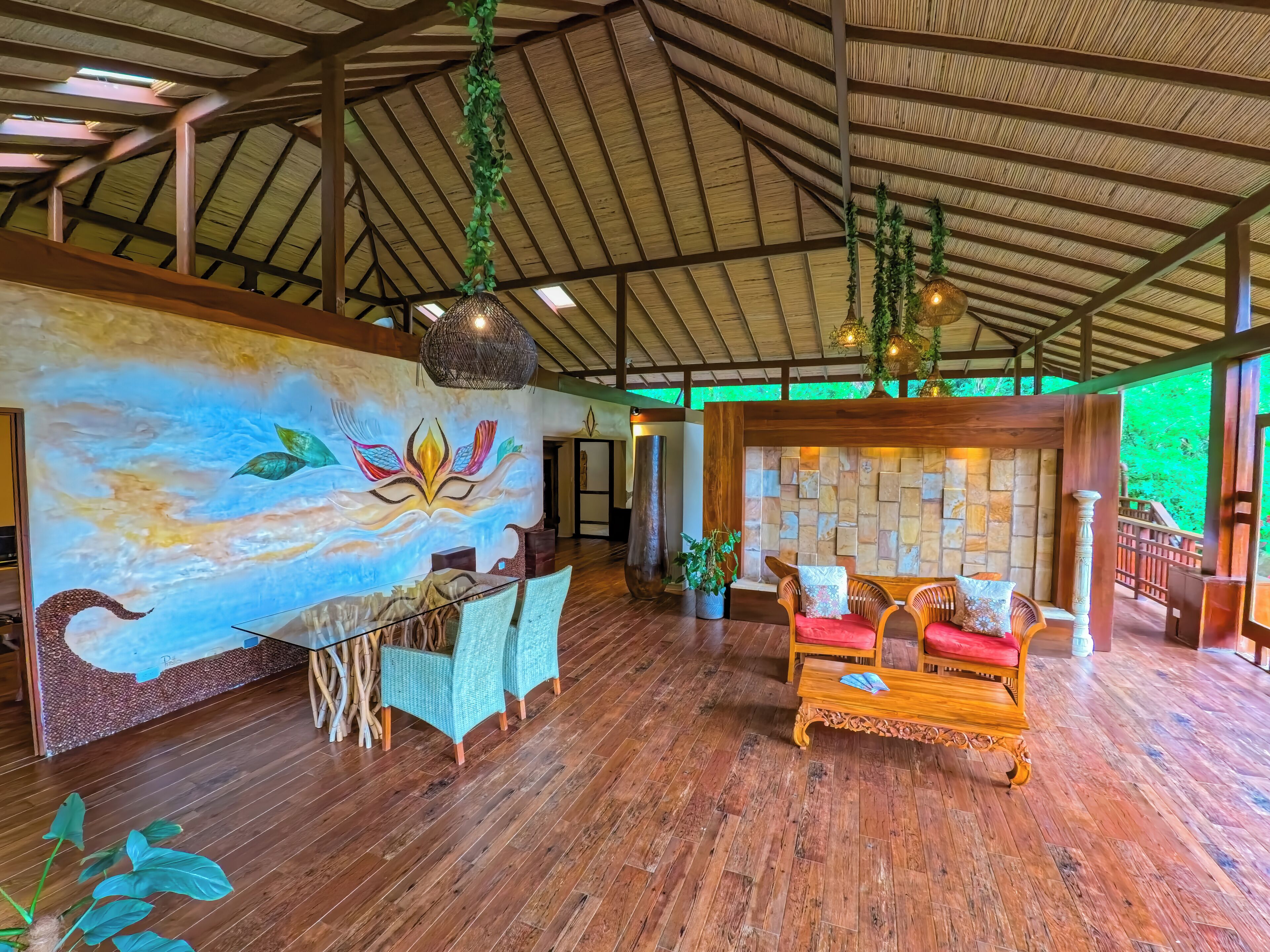 A spacious room with wooden floors, a mural, a dining area, and a seating area with a stone wall backdrop.