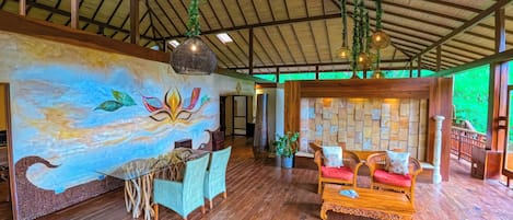 A spacious room with wooden floors, a mural, a dining area, and a seating area with a stone wall backdrop.