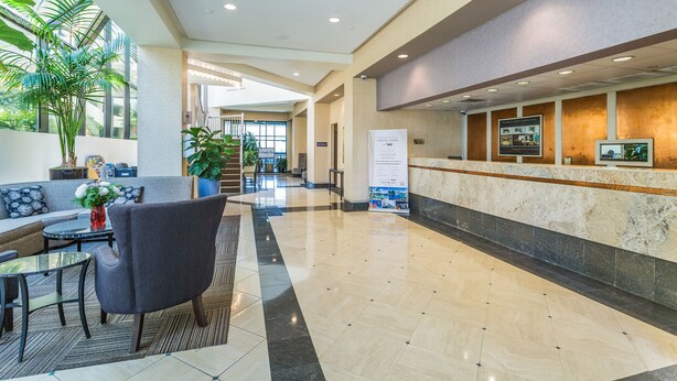 A hotel lobby with a reception desk, seating area, and large windows. - Beach Quarters Resort (Virginia Beach)