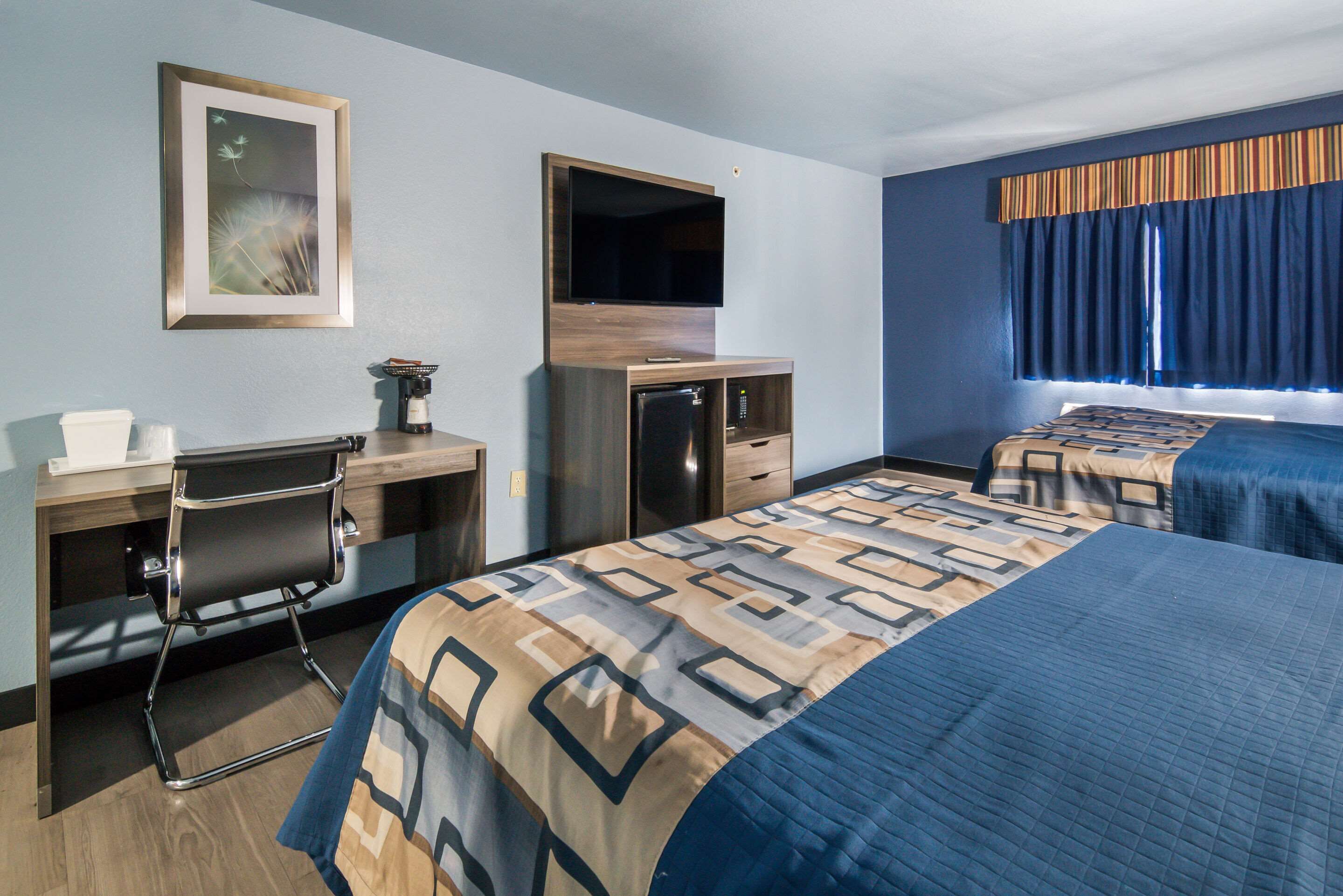 Une chambre d’hôtel avec un lit, un bureau, une chaise, une télévision et une fenêtre avec des rideaux.