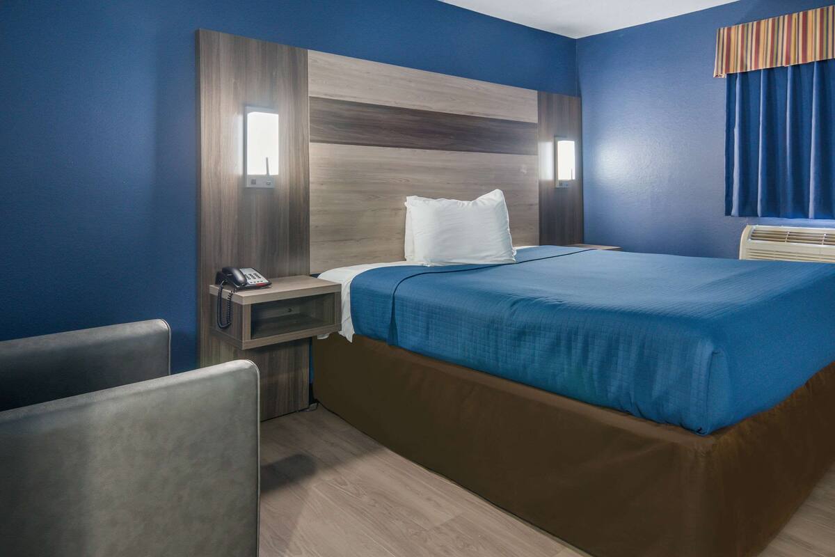 Una habitación de hotel con una cama grande, una mesita de noche con un teléfono y una silla.