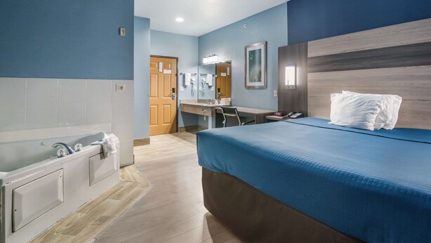 Habitación de hotel con una cama grande, baño independiente con bañera, escritorio y espejo.