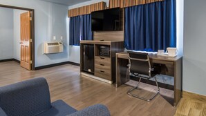 Una habitación de hotel con un escritorio de madera, televisor, una silla y un sofá.