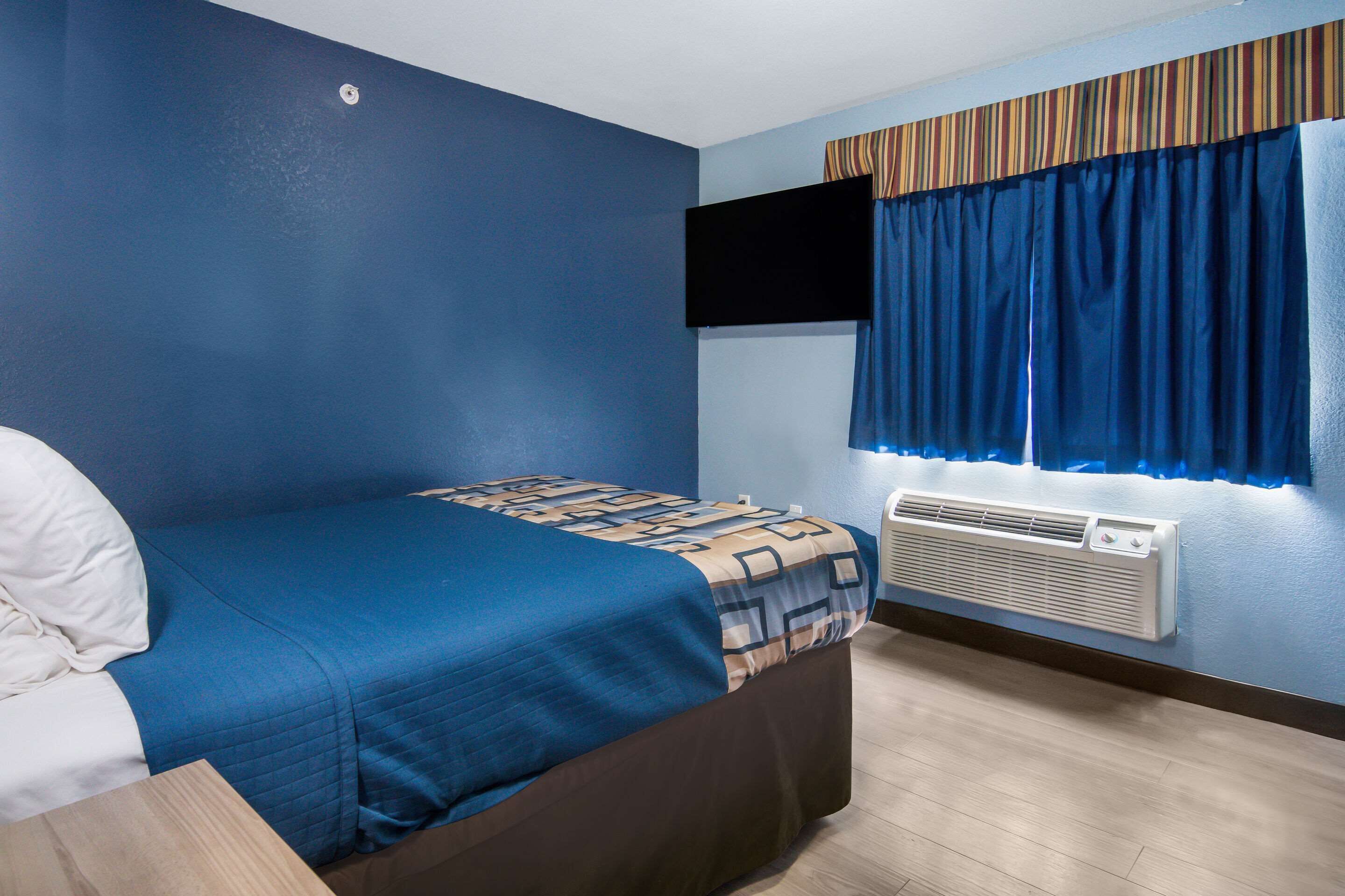Un dormitorio con cama, televisor de pantalla plana en la pared y aire acondicionado.
