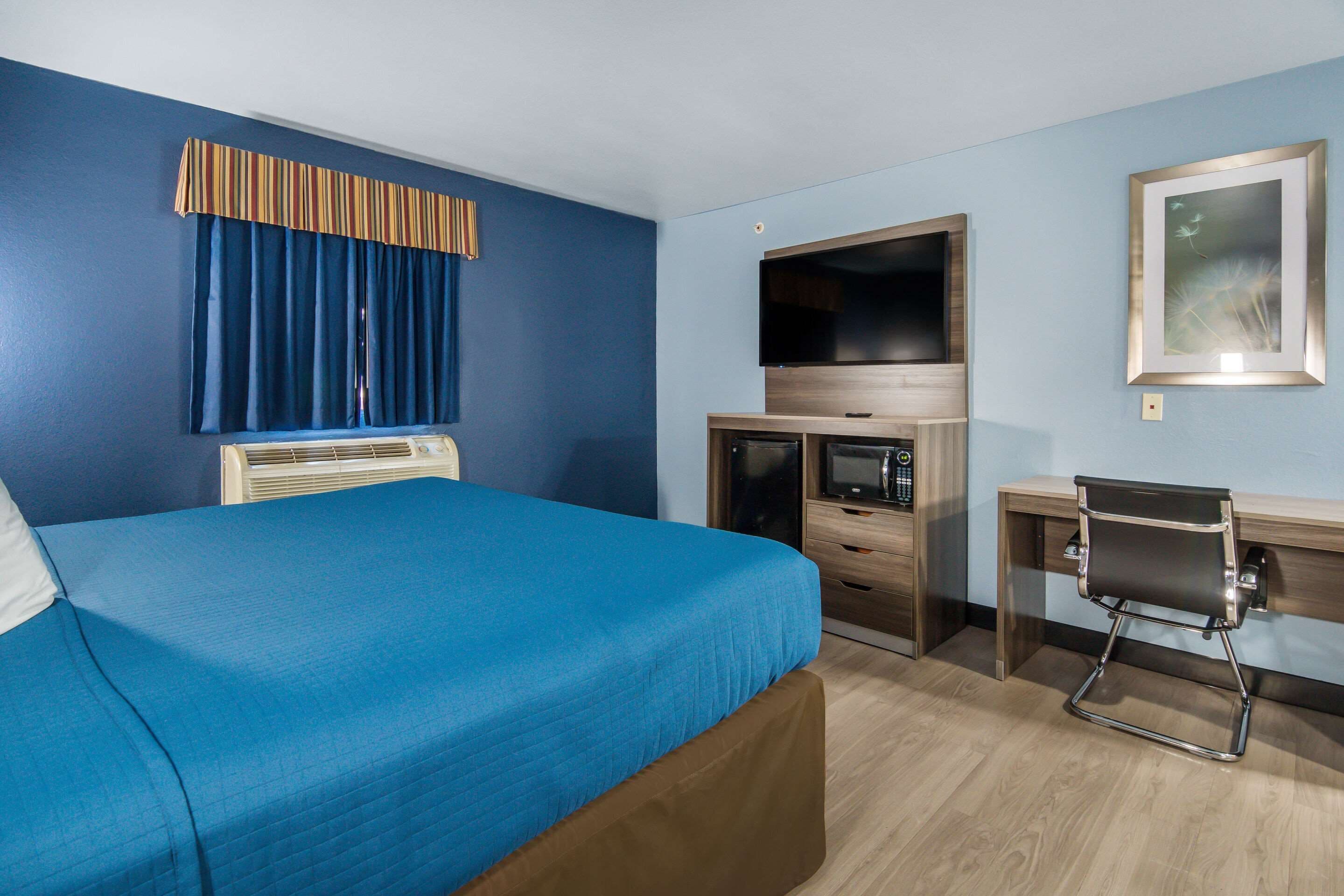 A hotel room with a bed, a desk, a chair, a television, and a window with curtains.