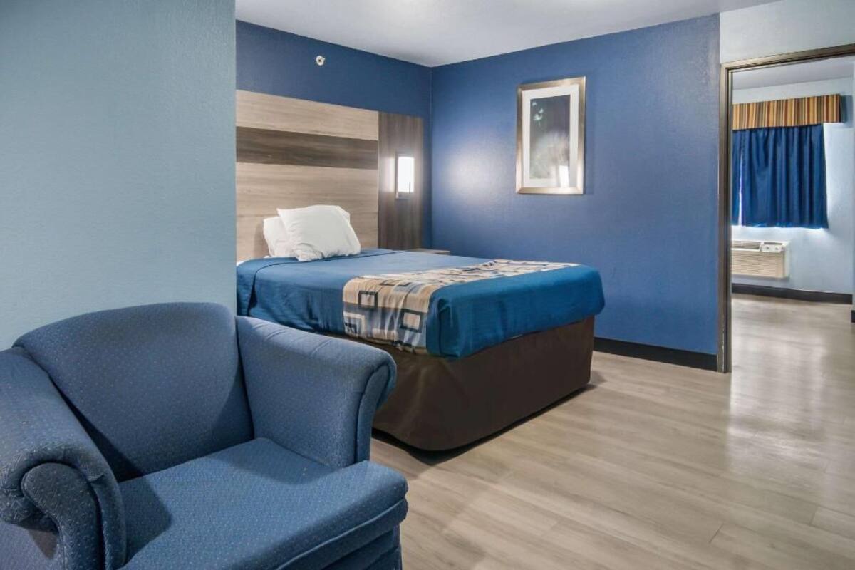Habitación de hotel con cama, una silla, un cuadro en la pared y una ventana con cortinas.
