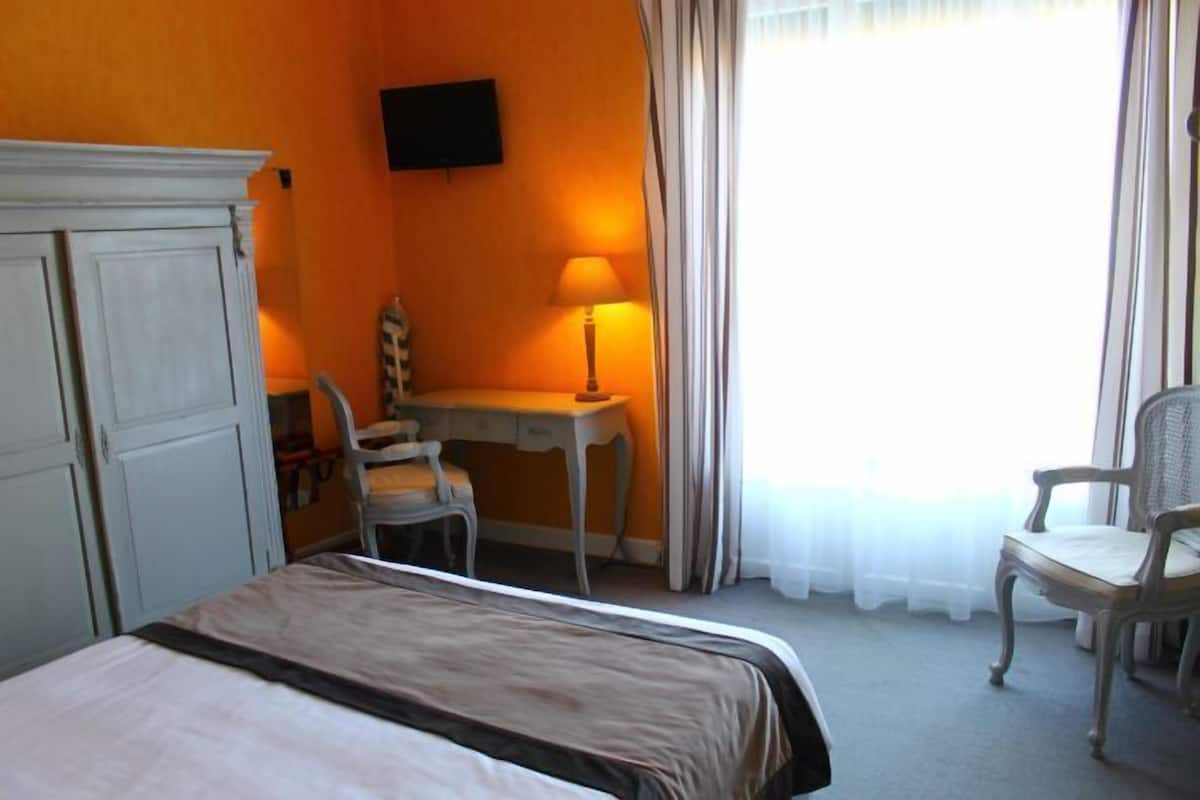 Ein Hotelzimmer mit einem Bett, einem Schreibtisch, einem Sessel, einem Fernseher und einem Fenster mit Vorhängen.