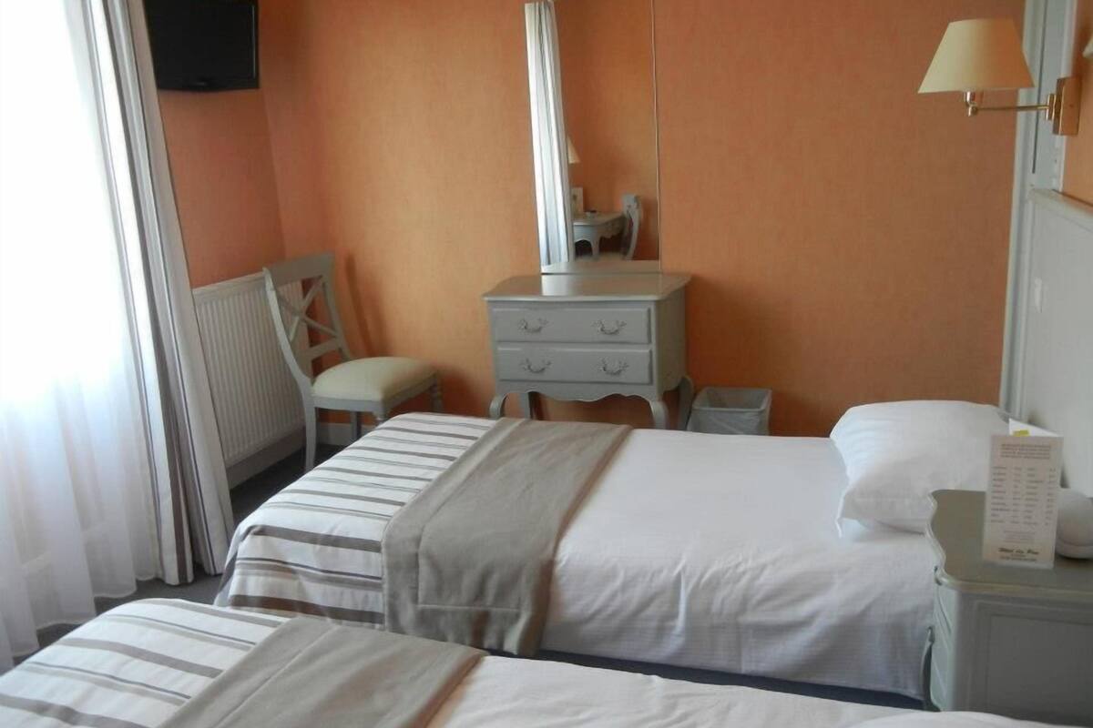 Ein Hotelzimmer mit zwei Betten, einem Schminktisch, einem Sessel, einem Spiegel, einer Lampe und einem Fernseher.