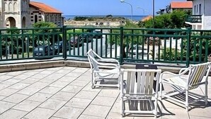 A terrace with white chairs and a table, overlooking a beach and a building with a red roof. - Hotel des Pins (Soulac-sur-Mer)