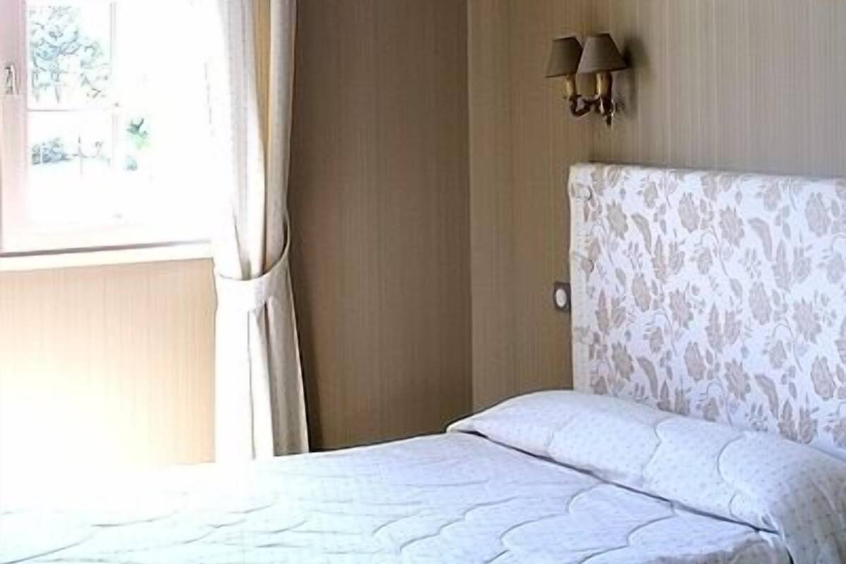 Ein Hotelzimmer mit Bett, einem fenster mit Vorhängen und einer Wandlampe.