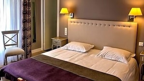 A hotel room with a large bed, two bedside lamps, a nightstand, a chair, and a window with curtains. - Hotel des Pins (Soulac-sur-Mer)