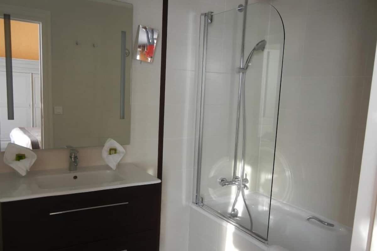 Ein modernes Badezimmer mit einer gläsernen Dusche, einem weißen Waschbecken und einer dunklen Ablagefläche.