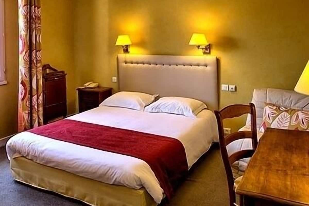 Ein Hotelzimmer mit einem Bett, zwei Nachttischlampen, einem Nachttisch, einem Holzstuhl und einem kleinen Tisch.