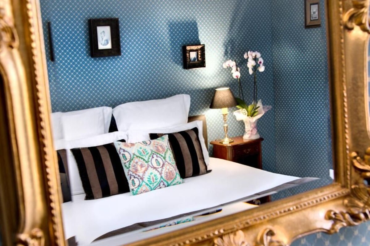 A bedroom with a bed, pillows, a nightstand, a lamp, and framed pictures on the wall.