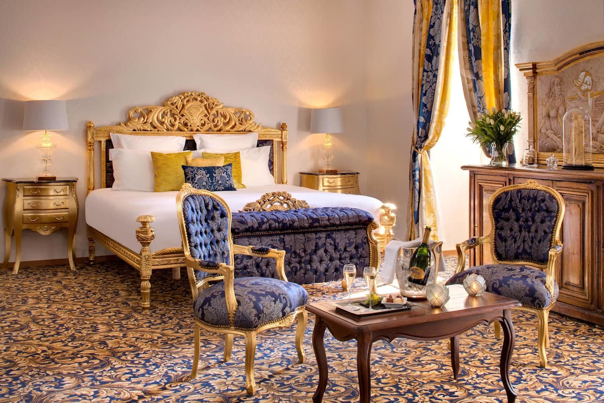 Une chambre à coucher luxueuse, dotée d’un grand lit, d’une tête de lit décorée et de fauteuils bleus assortis, recouverts d’un tissu élégant.