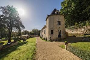 A stone building with a circular tower, surrounded by a gravel path and greenery.
