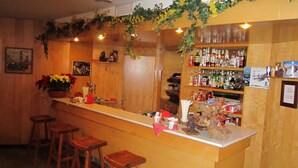 A bar area with wooden stools, a counter with various items, and shelves stocked with bottles. - Hotel de la Telecabine (Courmayeur)