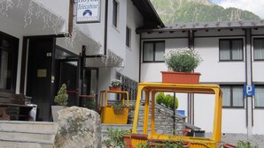 A hotel with a sign indicating it is a Courtyard Hotel. There are outdoor seating areas with yellow tables and potted plants. - Hotel de la Telecabine (Courmayeur)