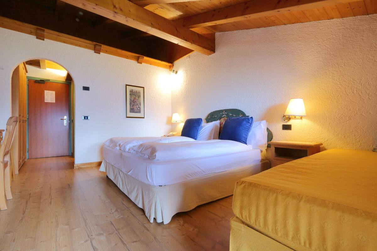Un dormitorio con techo de madera, cama con ropa de cama blanca, dos lámparas de noche y un banco de madera.