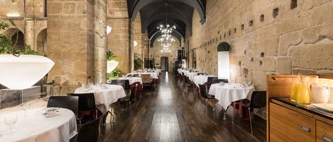 Un amplio comedor con mesas dispuestas para una comida, paredes de piedra y suelo de madera.