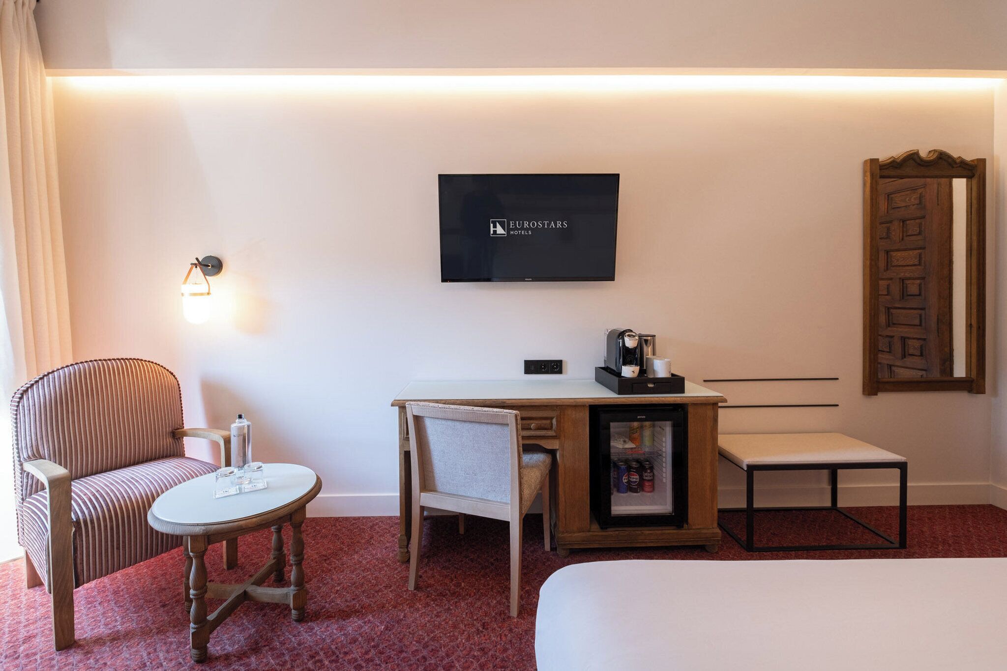 Une chambre d’hôtel comprenant un lit, un bureau avec une machine à café, un téléviseur affichant le logo « Eurostars Hotels », une chaise et une petite table.