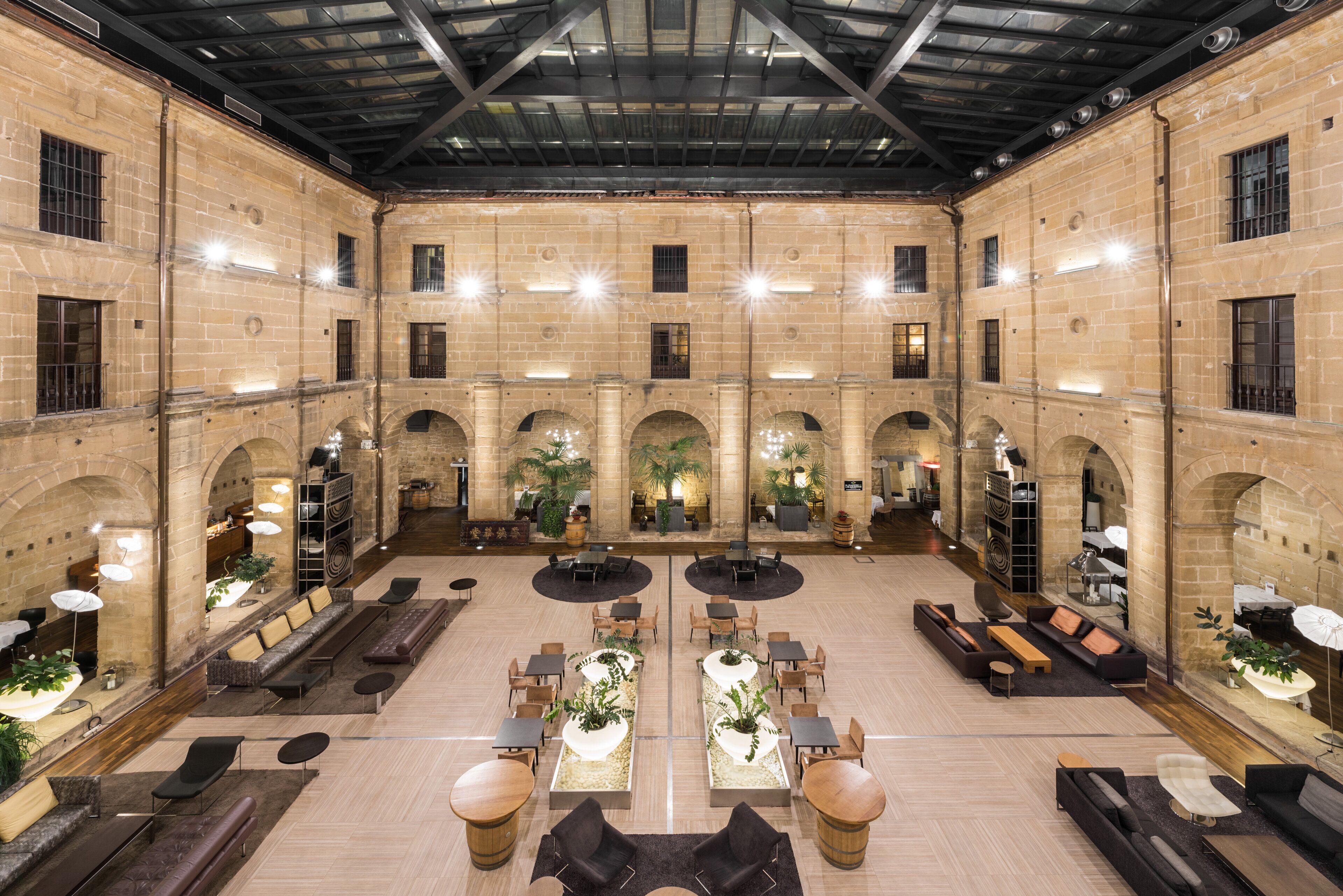 A spacious lobby with high ceilings, arched walkways, and a central seating area with tables and chairs.