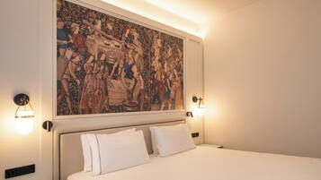 Een hotelkamer met een groot wandtapijt, een bed met witte lakens en wandlampen.