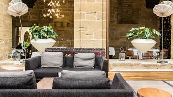 A cozy seating area with a sofa and armchairs, surrounded by stone walls and a chandelier.