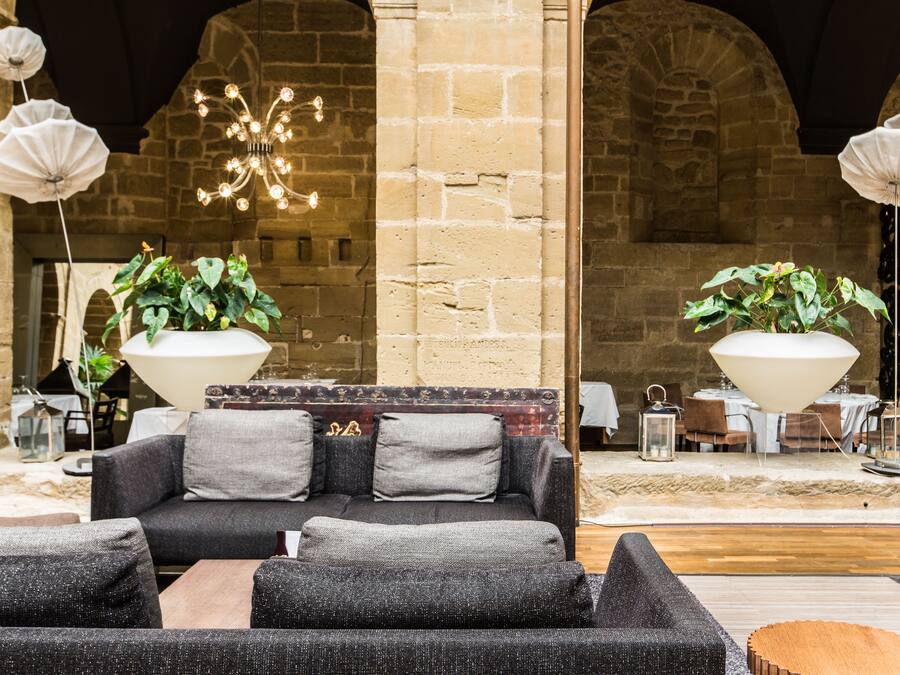 A cozy seating area with a sofa and armchairs, surrounded by stone walls and a chandelier.