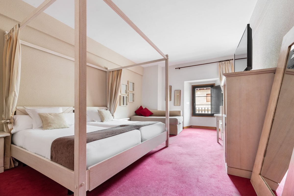 Ein Bett mit Baldachin und Holzrahmen, ein roter Teppich und ein Holzkleiderschrank.