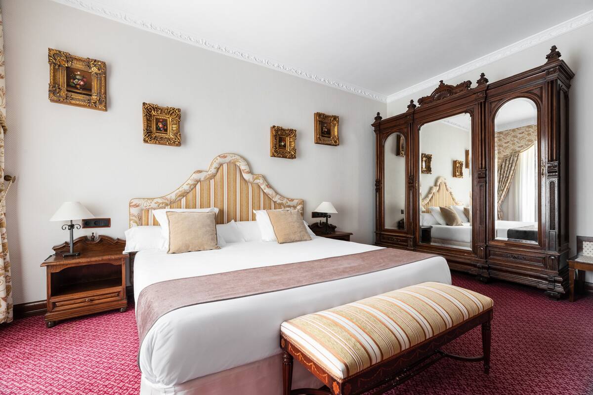Ein Hotelzimmer mit einem großen Bett, zwei Nachttischen mit Lampen, einer Holzbank und einem großen Spiegel.