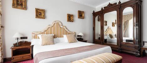 A hotel room with a large bed, two bedside tables with lamps, a wooden bench, and a large mirror.