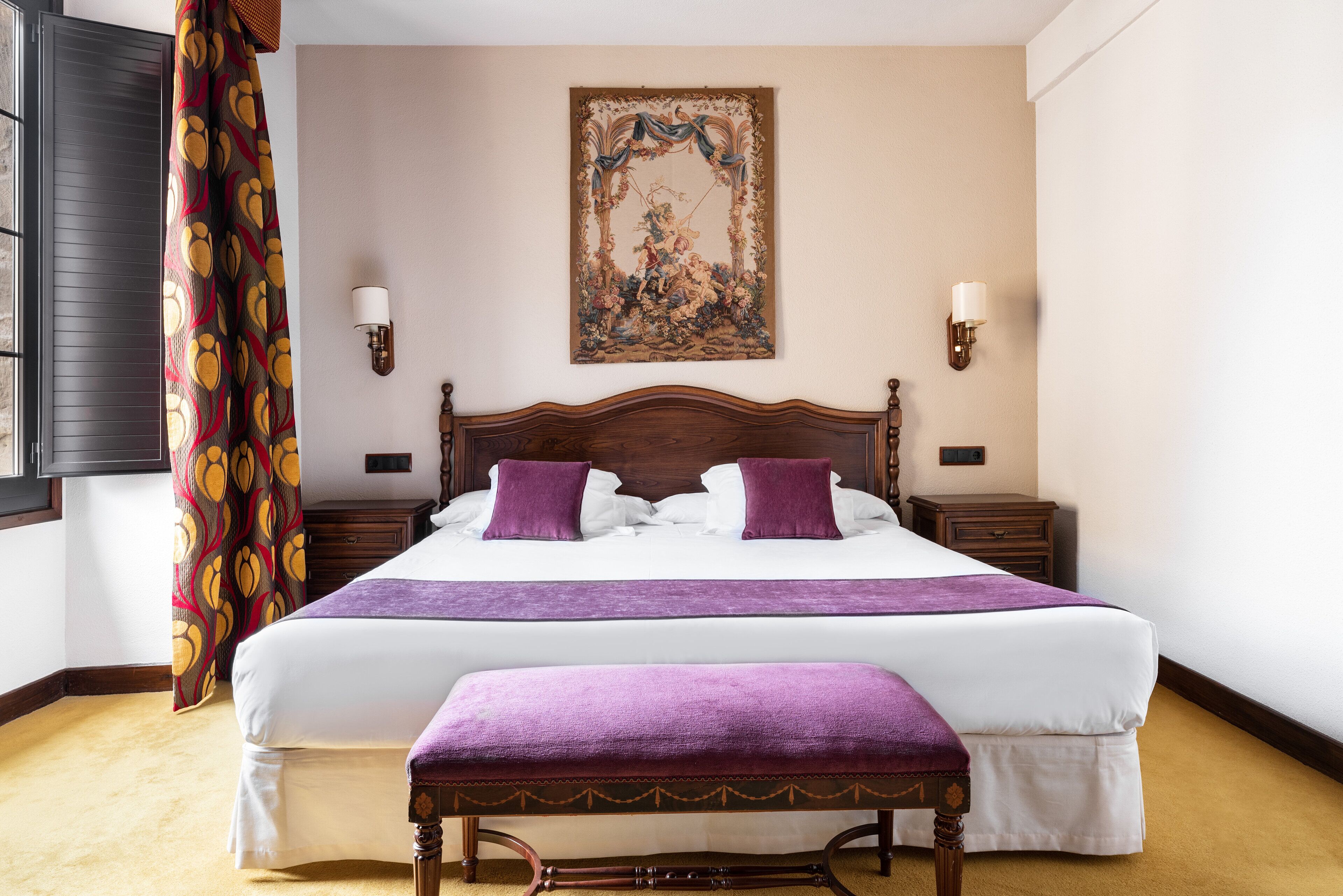 Una cama bien hecha con una colcha y almohadas moradas, un cabecero de madera y un banco al pie de la cama.
