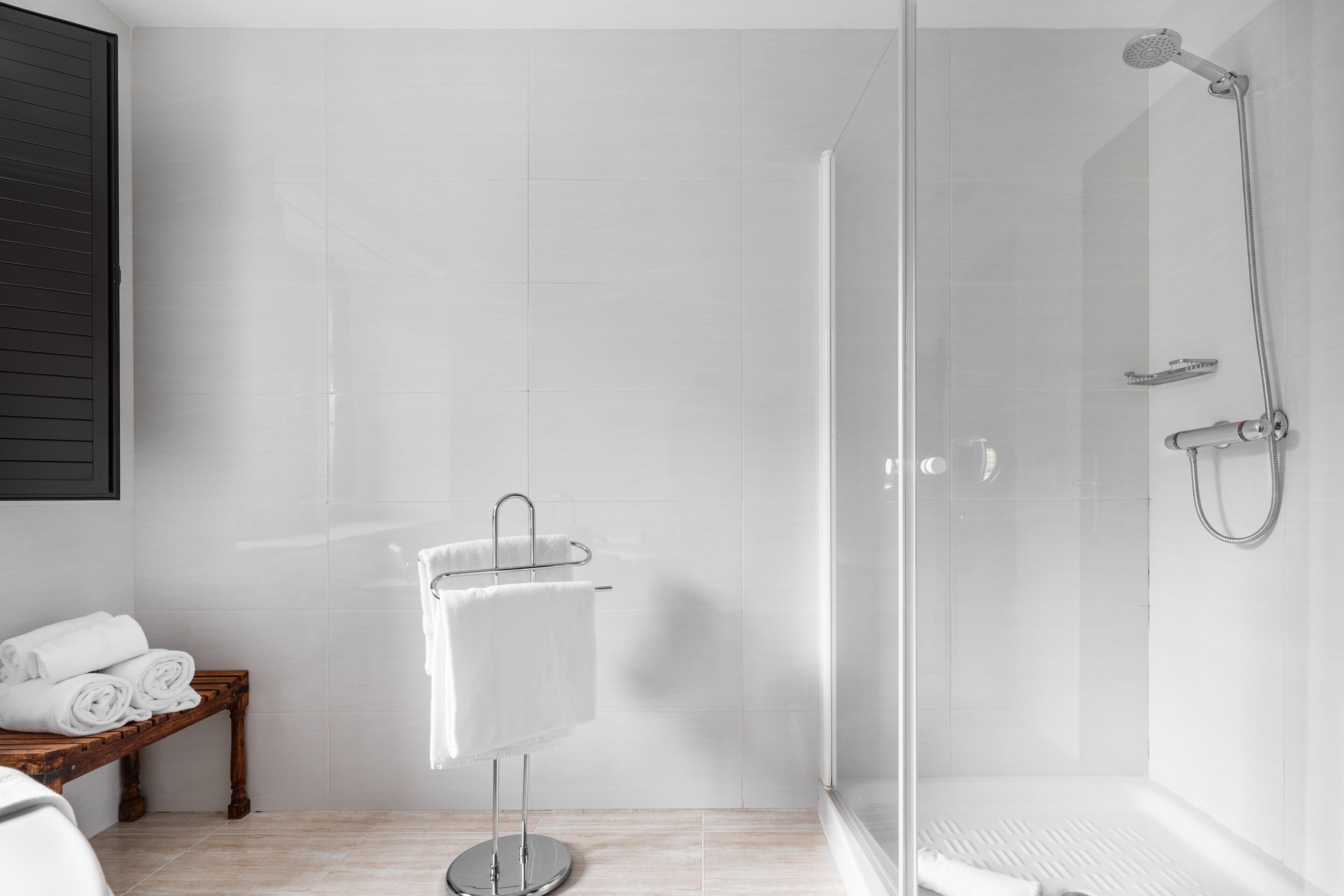 Une salle de bain moderne avec une douche à parois de verre, un banc en bois avec des serviettes et un porte-serviettes fixé au mur.