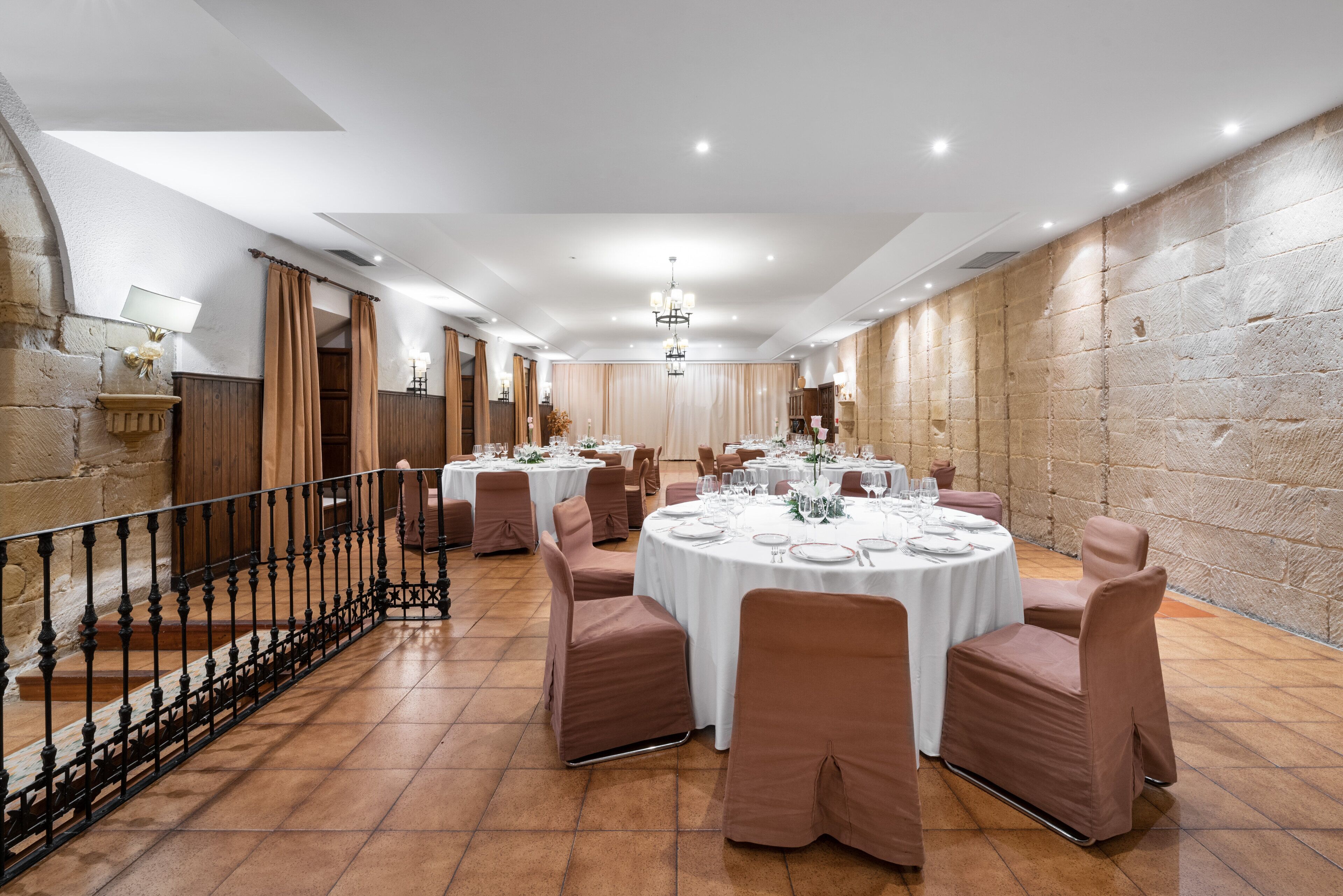 A banquet hall with round tables, brown chairs, and a stone wall.