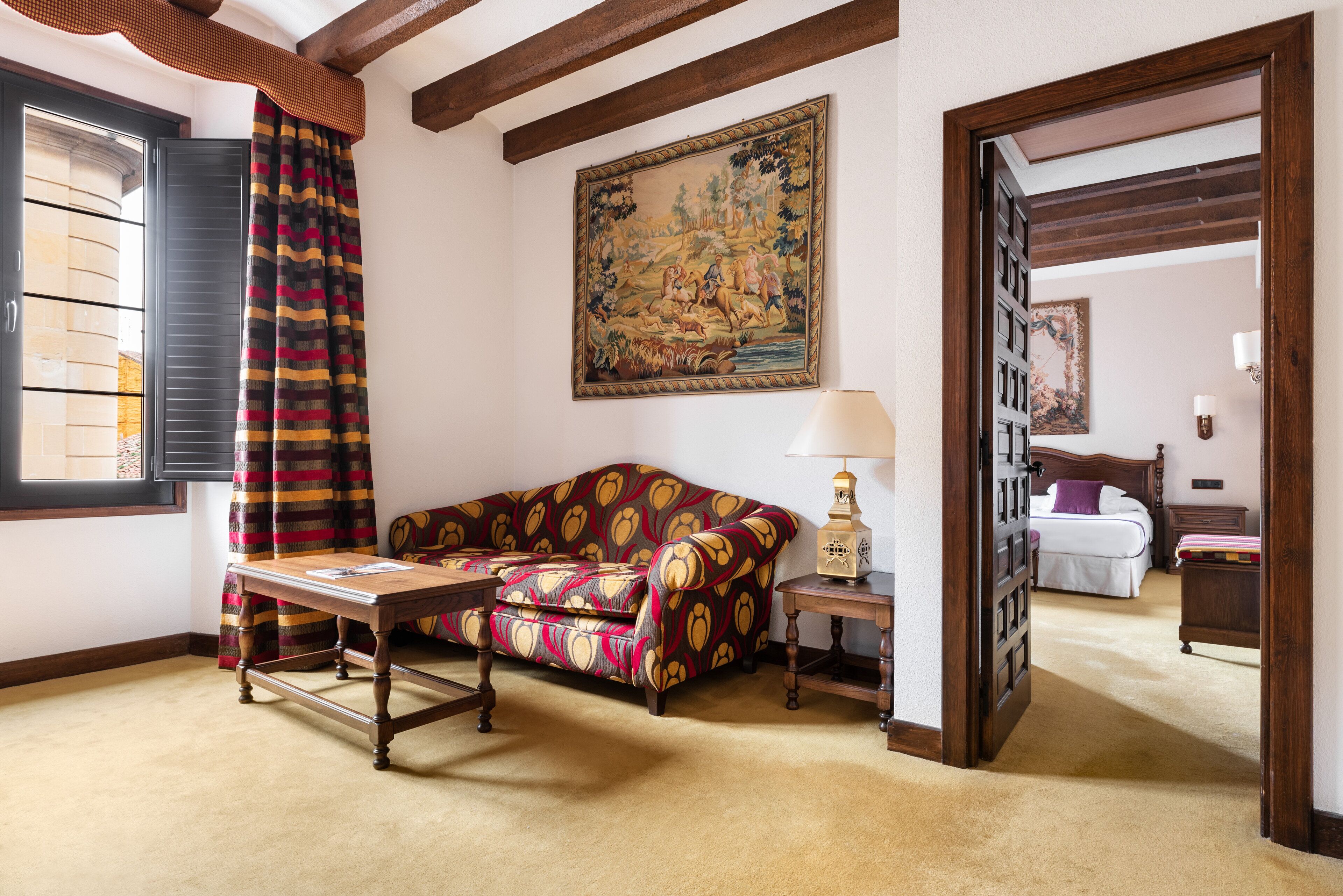 Una habitación con un sofá estampado, una mesa de madera, una lámpara y un cuadro en la pared.