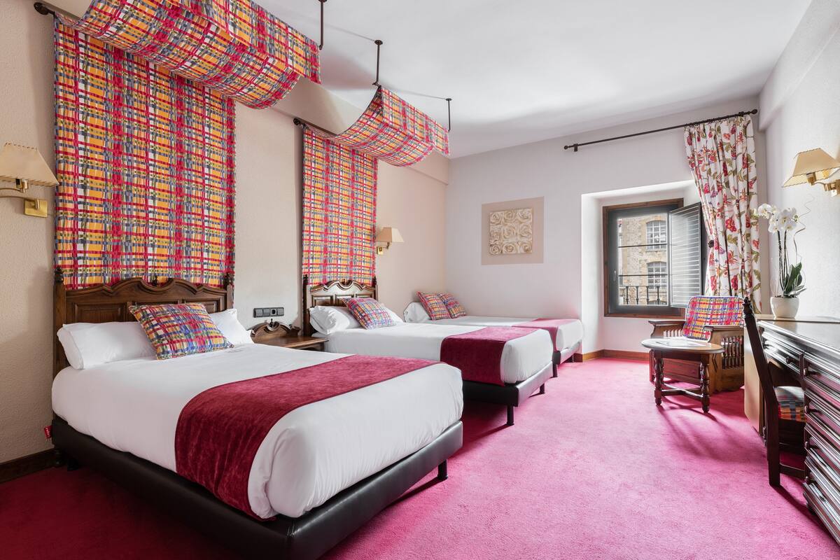 Ein Hotelzimmer mit zwei Betten, einem Schreibtisch, einem Stuhl und einem Fenster mit Vorhängen.