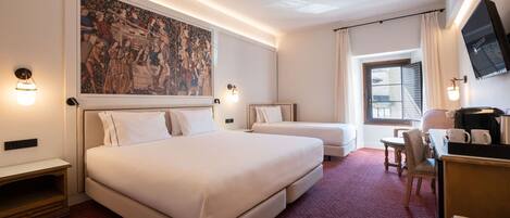 Habitación de hotel con una cama grande, una cama más pequeña, un escritorio con silla, televisión y un cuadro en la pared.