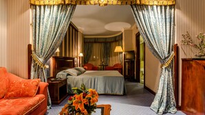A hotel room with a large bed, a sofa, a nightstand, a lamp, and a vase with flowers. - Hotel Infanta Cristina (Jaén)